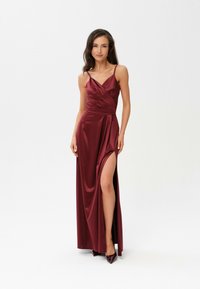 Burgundská saténová róba s drapovaným designem, tenkými ramínky, vysokým rozparkem a přiléhavým pasem. V doprovodu odpovídajících špičatých lodiček.