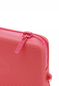 Custodia rosa con zip realizzata in materiale gommoso testurizzato con un motivo a nido d'ape, dotata di un tirazip abbinato e un dettaglio con logo.