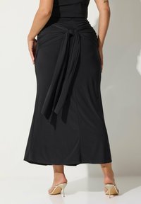 Gonna maxi nera con dettaglio in vita annodato, texture liscia e silhouette fluida, abbinata a scarpe con tacco alte beige.
