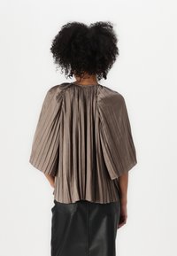 Faltendes Oberteil aus weichem Taupe-Stoff mit weiten Ärmeln und gerafftem Ausschnitt, das eine glatte Textur und eine fließende Silhouette aufweist.