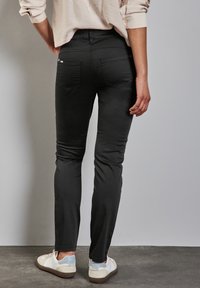 Schwarze Skinny Jeans mit hoher Taille, hinteren Taschen und glatter Stoffstruktur, kombiniert mit weißen Sneakern.