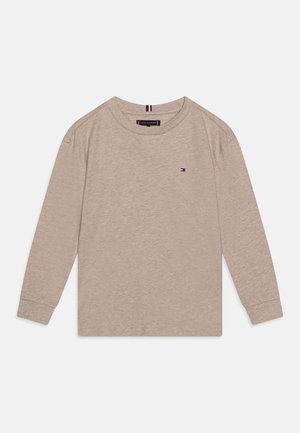 Chemise beige à manches longues avec col rond, petit logo Tommy Hilfiger sur la poitrine et étiquette intérieure au col avec le nom de la marque.