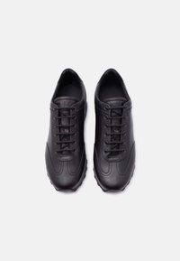 Paire de baskets basses en cuir noir avec lacets, bouts arrondis, présentées côte à côte sur un fond blanc uni.