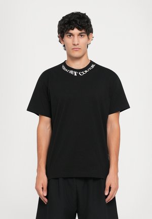 Sort t-skjorte i svart bomull med rund hals, og hvit "Versace Jeans Couture" tekst. Løs passform, korte ermer, og minimalistisk design.