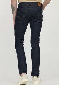 Jean skinny en denim noir avec des coutures orange, design à cinq poches, étiquette en cuir à la taille et légère élasticité pour le confort.
