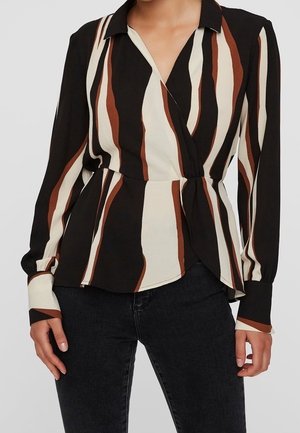 Femme portant un chemisier portefeuille à manches longues avec des rayures verticales noires, blanches et marron, associé à un jean noir.