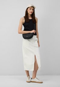 Zwarte tanktop, witte denim midi-rok met een vooruitsnijding, zwarte crossbody tas, beige sneakers met zwarte accenten en een lichtgekleurde pet.