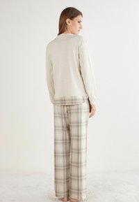 Top de manga larga gris claro combinado con pantalones de pijama a rayas beige que presentan acentos en azul y marrón, con tela suave y un ajuste relajado.