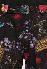 Zwarte stoffen broek met levendige bloemen- en insectenpatronen. Voorzien van een decoratieve zilveren gesp en kleurrijke accenten op de tailleband.