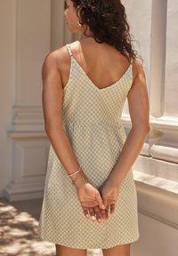 Robe en vichy vert clair avec un corsage ajusté et une jupe évasée. Dos en V et fines bretelles réglables. Tissu à texture lisse.