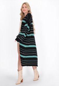 Musta ja turkoosi raidoitettu pitkä kardigan, jossa avoin etuosa, kevyt neulostekstuuri ja leveät hihat. Päällä beige paita.