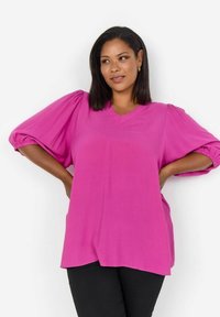 Rosa V-Ausschnitt-Bluse mit kurzen Puffärmel, aus einem glatten Stoff gefertigt; zeichnet sich durch einen entspannten Schnitt und einen leicht geschwungenen Saum aus.