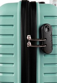 Maleta rígida de color verde menta con relieves verticales, cremallera y cerradura negras, detalles de herrajes plateados y superficie texturizada.