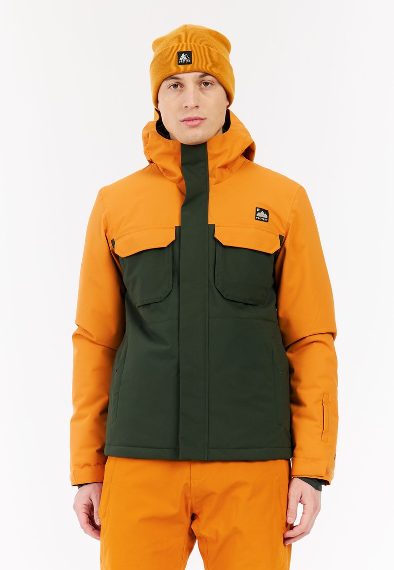 Oranžová a tmavozelená zateplená bunda s kapucňou, dvoma veľkými náprsnými vreckami a logom na hornej ľavej strane. Nosí sa s oranžovými nohavicami.