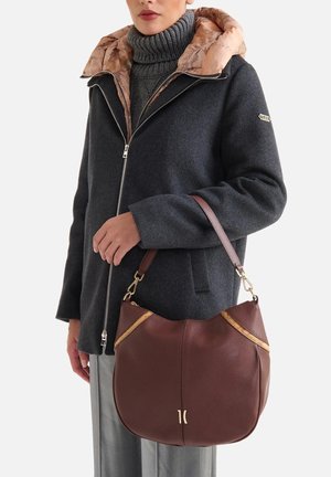 Borsa a mano in pelle marrone con dettagli dorati, forma curva e design bicolore; abbinata a un cappotto scuro e un dolcevita grigio.