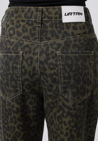 Camouflage leopard-print jeans in dark green and black denim, featuring two back pockets and a white label with "URTRN" logo on waistband.