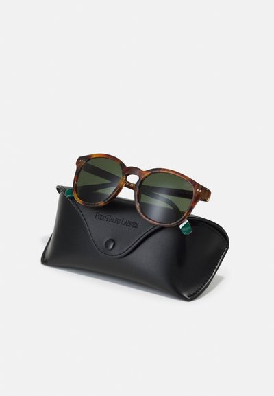 Brune skilpadde-solbriller med mørkegrønne linser, som hviler på et svart lærdeksel med trykknapp og preget merkevare.