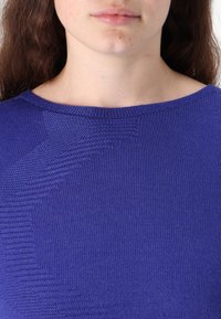 Top tricotat cu maneci scurte de culoare purpurie, cu un model texturat și un guler rotund, având un finisaj neted și o variație subtilă a culorii.