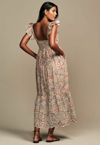Abito maxi floreale con maniche a volant, design senza schienale, base beige e accenti rossi/neri. Realizzato in tessuto leggero con vita arricciata.
