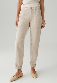 Pantaloni beige con una vestibilità comoda, dotati di vita alta, tasche frontali e orli arrotolati, abbinati a scarpe piatte beige.
