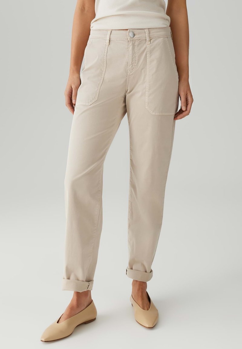 Pantaloni beige con una vestibilità comoda, dotati di vita alta, tasche frontali e orli arrotolati, abbinati a scarpe piatte beige.