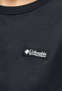 Κοντινό πλάνο μαύρου υφάσματος με μια μικρή ραμμένη μαύρη ετικέτα που δείχνει λευκό λογότυπο και κείμενο «Columbia Sportswear Company».