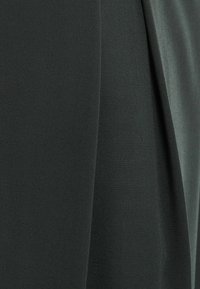 Mörkgrön tyg med en texturerad yta, som har släta och lätt draperade sektioner för en lagerlook. Inga synliga mönster eller hårdvara.