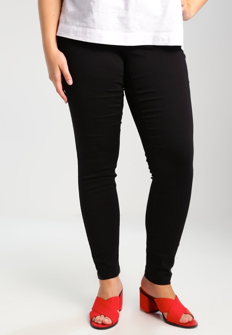 Jean skinny noir associé à des sandales rouges à talons blocs. Le jean présente une texture lisse, et les sandales ont un design à bride croisée.