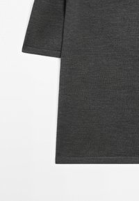 Manche courte de chemise gris foncé et panneau latéral sur fond blanc montrant la texture du tissu et la couture de l'ourlet.