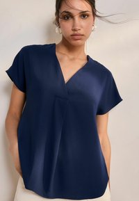 Blusa a manica corta blu navy con scollatura a V, texture morbida e vestibilità leggermente ampia. Presenta un sottile dettaglio della cucitura frontale.