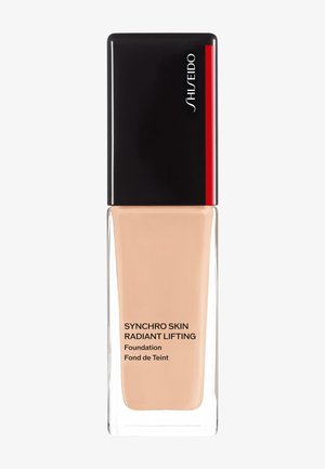 Shiseido Synchro Skin Radiant Lifting foundation in a clear glass bottle with a black cap and red accent, displaying light beige liquid.