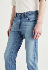 Ljusblå denimjeans med rak passform, ljus tvätt och subtila slitningar, med en metallknapp och femfickorsdesign.