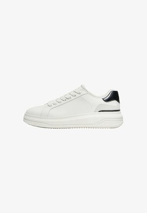 Basket basses blanches avec lacets à l’avant et détail noir au talon sur une semelle épaisse, vues de côté sur fond blanc.