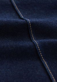 Tissu denim bleu foncé plié pour mettre en valeur les coutures orange proéminentes le long des coutures, montrant la texture et les détails du matériau.