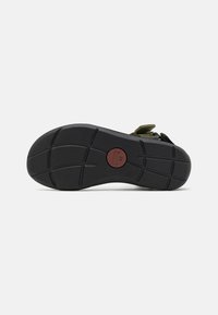 Suela de zapato de goma negra con un patrón texturizado y un emblema rojo circular. Presenta ranuras para tracción y un indicador de tamaño (42).