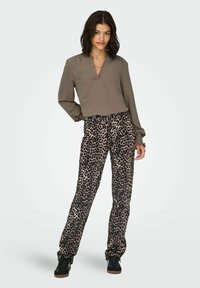 Maslinasto zeleni bluz sa V-izrezom i nabranim rukavima uparen s trapezicama u leopardskom uzorku u bež i crnoj boji. Crne tenisice upotpunjuju look.