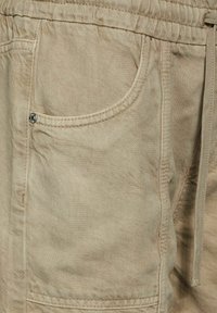 Pantalones cortos de algodón en color beige con una cintura elástica, que cuentan con un bolsillo lateral, costuras visibles y un acabado suave, ligeramente texturizado.