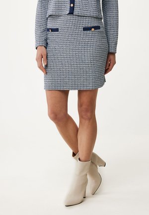 Jupe à carreaux bleus et blancs avec deux poches navy et des boutons dorés, associée à des bottines crèmes à bout pointu et talon bloc.