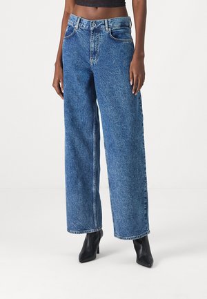 Blauwe wijde denim jeans met een hoge taille, voorzien van een klassieke vijf-pocketontwerp en subtiele vervaging. Gecombineerd met zwarte puntige hakken.