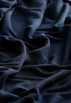 Marineblauwe stof in zachte plooien gedrapeerd, met een gladde textuur en een gelijkmatige oppervlakte, waarbij zachte golven en schaduwen te zien zijn.