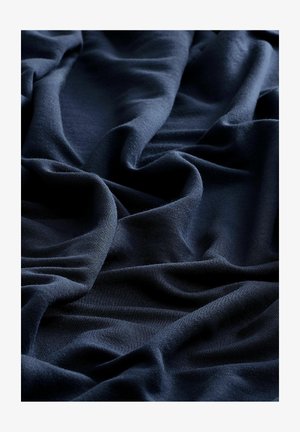 Marineblåt stof draperet i bløde folder med en glat tekstur og en ensartet overflade, der viser blide bølger og skygger.