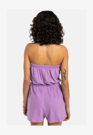 Lilla õlakarvaita kombinesoon elastse vöödiga ja lühikeste pükstega, millel on mugav lõige ja pehme tekstuur. Tagantvaates ei ole täiendavaid detaile.