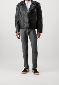 Černá kožená motorkářská bunda se zipy, v kombinaci se šedými úzkými kalhotami a černými teniskami s gumovou podrážkou a bílými detaily.