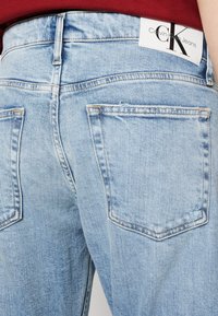 Jeans in denim azzurro con vita alta, due tasche posteriori e un'etichetta bianca visibile con "Calvin Klein Jeans" e un logo.