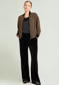 Bronzefarbene Pailletten-Bomberjacke mit schwarzem Besatz, kombiniert mit schwarzen, weiten Samthosen. Das Outfit zeichnet sich durch eine lockere Passform und Taschen aus.