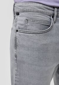 Vaqueros de denim gris con una textura suave, que cuentan con un bolsillo trasero, costuras sutiles y una etiqueta de logo negra en la cintura.