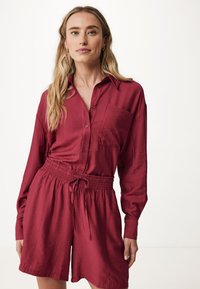 Rotes, langärmliges Hemd mit Knöpfen und einer Tasche, kombiniert mit passenden Shorts mit elastischem Bund und Zugband. Glatte Textur.