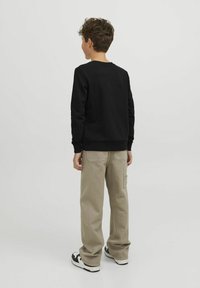 Felpa nera con maniche lunghe, polsini e orlo a coste; abbinata a pantaloni cargo beige. Presenta sneakers con dettagli neri e bianchi.