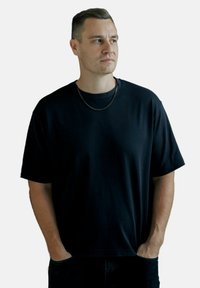 Sort bomulds t-shirt med rund hals og korte ærmer, med en afslappet pasform og glat tekstur. Inkluderer en subtil sølv kæde-smykke.