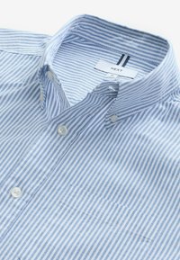 Chemise boutonnée à rayures bleu clair et blanches avec un col, dotée de boutons ronds et d'un détail de poche. Le tissu semble doux et texturé.